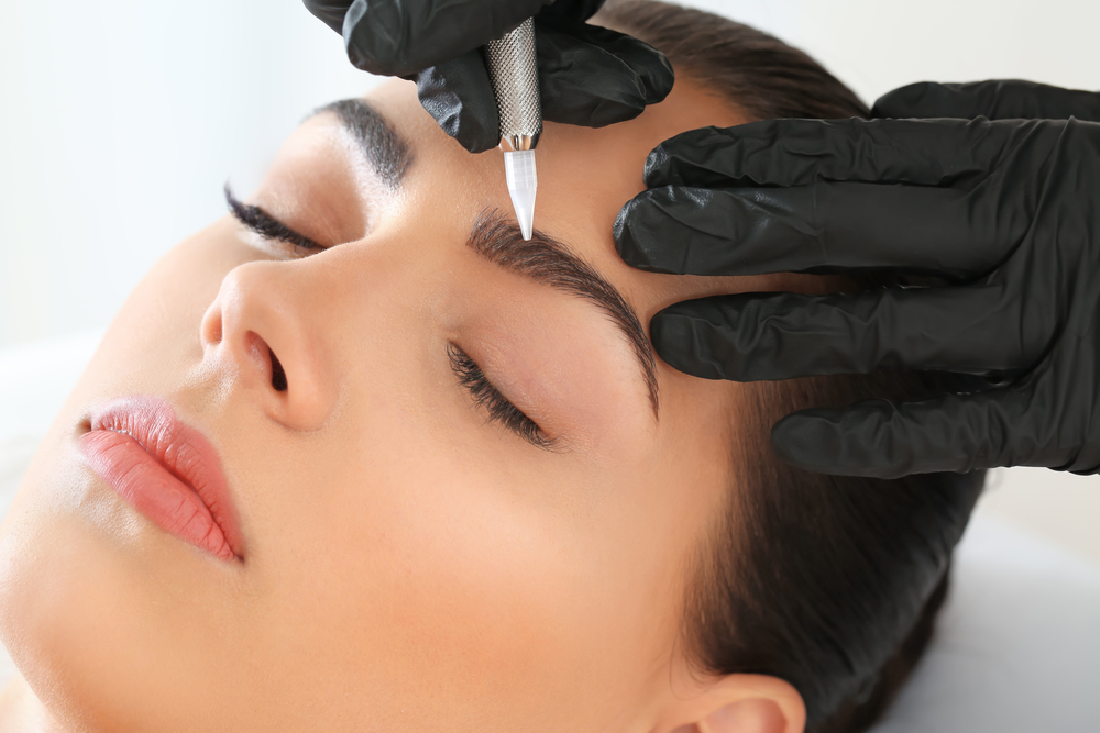 Young woman undergoing procedure of eyebrow permanent makeup in beauty salon, closeup