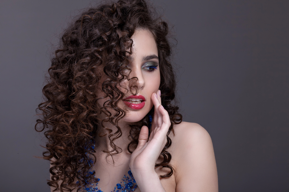 Woman with soft, defined brunette curls showcasing modern perm hairstyle trends in Aliquippa, PA.