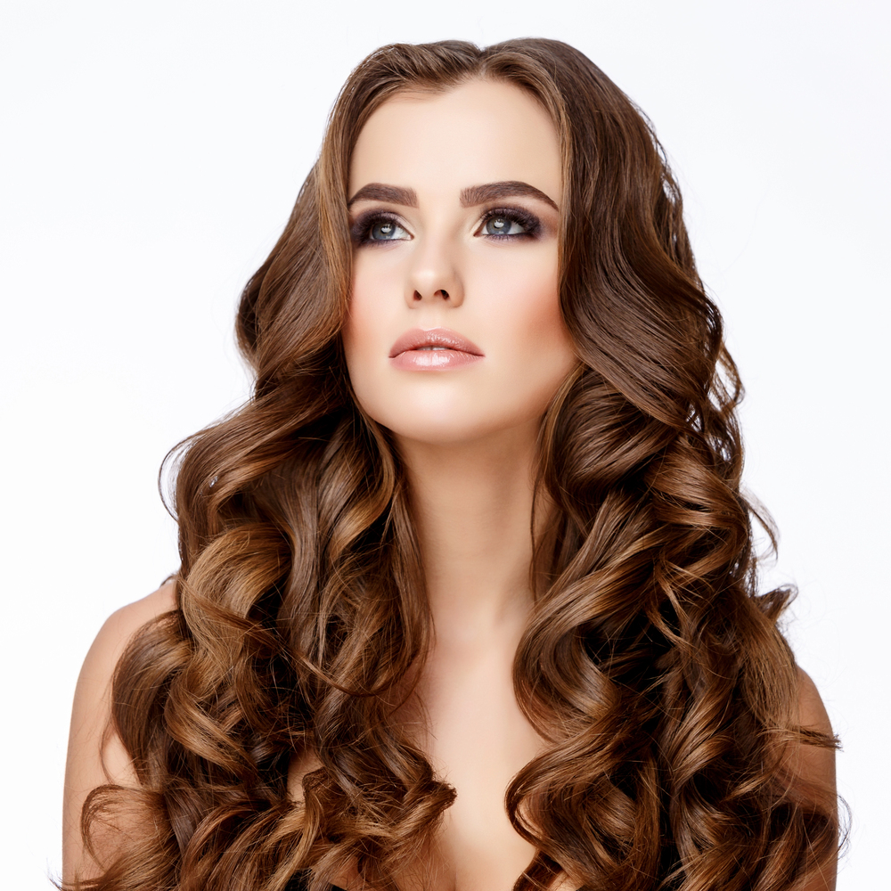 Woman with long, voluminous wavy brunette hair featuring warm brown tones and soft caramel highlights.